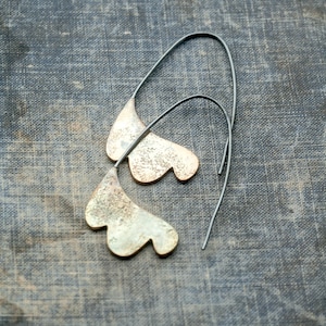 May include: A pair of silver earrings with a unique, organic shape. The earrings are made of metal and have a textured surface. They hang from thin silver wires.