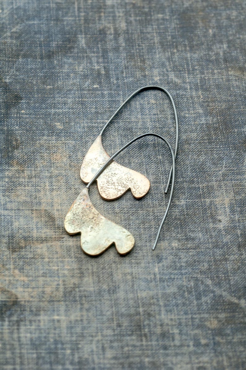 May include: A pair of silver earrings with a unique, organic shape. The earrings are made of metal and have a textured surface. They hang from thin silver wires.