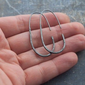 Pu&ograve; includere: Un paio di orecchini a cerchio ovali neri. Gli orecchini sono in metallo e hanno una texture martellata.