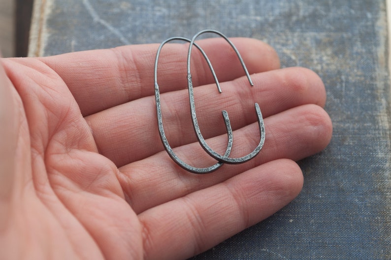 Pu&ograve; includere: Un paio di orecchini a cerchio ovali neri. Gli orecchini sono in metallo e hanno una texture martellata.