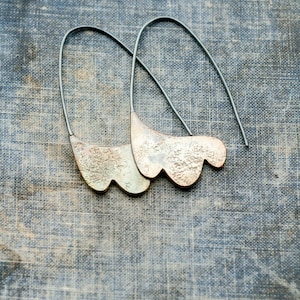 May include: A pair of silver earrings with a textured, organic shape. The earrings are suspended from thin silver wires.