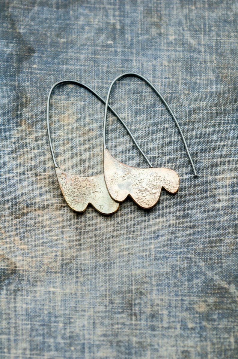 May include: A pair of silver earrings with a textured, organic shape. The earrings are suspended from thin silver wires.