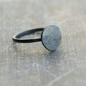 May include: A silver ring with a round, textured top. The ring is made of metal and has a simple design.
