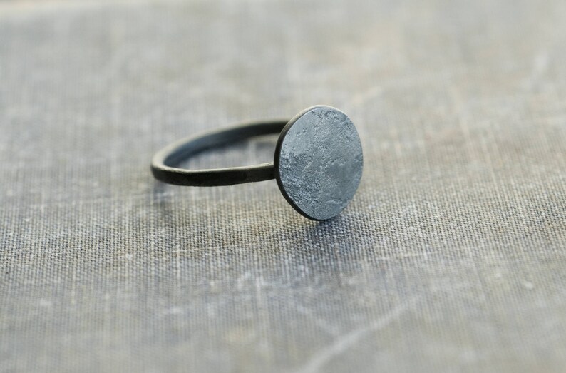 May include: A silver ring with a round, textured top. The ring is made of metal and has a simple design.