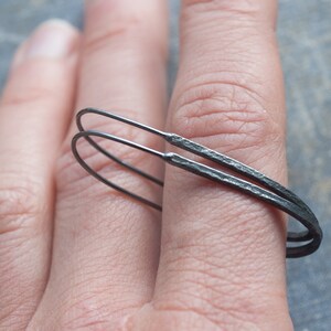 Pu&ograve; includere: Un paio di orecchini a cerchio neri con una texture martellata. Gli orecchini sono in metallo e vengono indossati sull'orecchio di una persona.