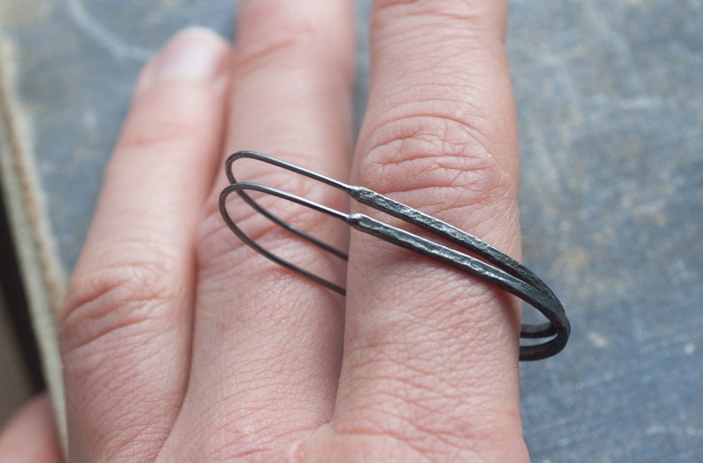 Pu&ograve; includere: Un paio di orecchini a cerchio neri con una texture martellata. Gli orecchini sono in metallo e vengono indossati sull'orecchio di una persona.