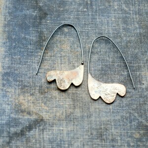 May include: A pair of silver earrings with a textured, organic shape. The earrings are suspended from thin black wires.