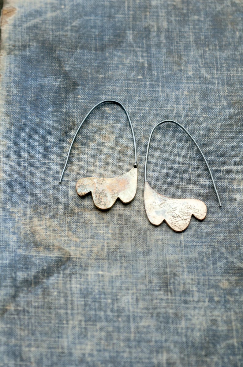 May include: A pair of silver earrings with a textured, organic shape. The earrings are suspended from thin black wires.