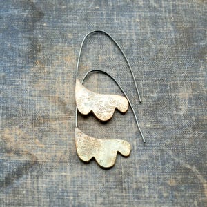 May include: A pair of silver earrings with a unique, organic shape. The earrings are made of metal and have a textured surface.