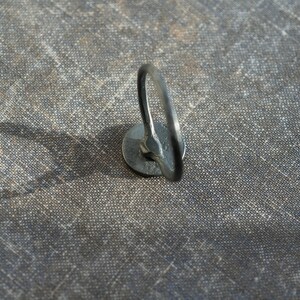 May include: A close-up of a silver metal ring attached to a fabric surface. The ring is circular and has a smooth finish.