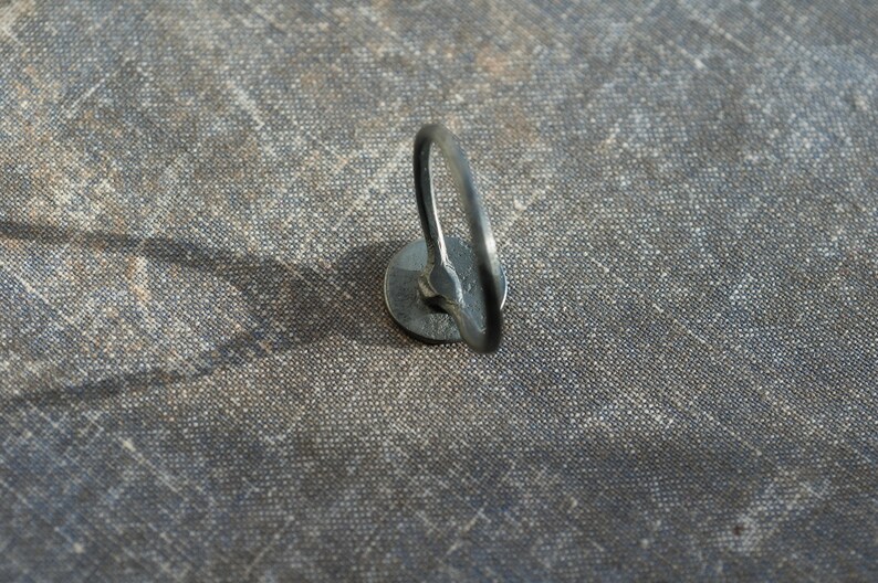 May include: A close-up of a silver metal ring attached to a fabric surface. The ring is circular and has a smooth finish.