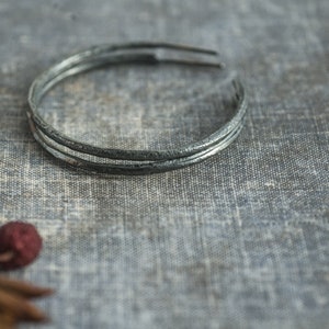 Puede incluir: Un brazalete de plata con acabado martillado. El brazalete está hecho de tres bandas finas de metal.