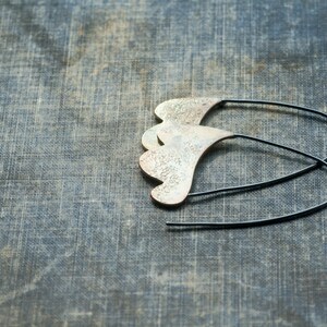 May include: A pair of silver earrings with a unique, organic shape. The earrings are made of metal and have a textured surface. The earrings are hanging from a black wire.