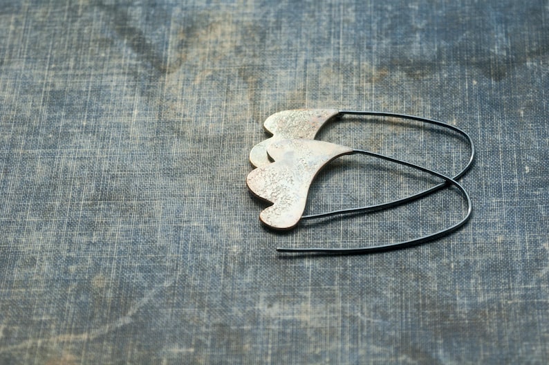 May include: A pair of silver earrings with a unique, organic shape. The earrings are made of metal and have a textured surface. The earrings are hanging from a black wire.