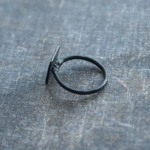 Puede incluir: Un anillo negro con una banda de forma cuadrada. El anillo es de metal y tiene un dise&ntilde;o sencillo.