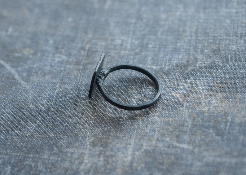 Puede incluir: Un anillo negro con una banda de forma cuadrada. El anillo es de metal y tiene un dise&ntilde;o sencillo.
