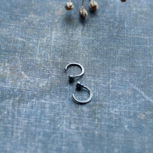 May include: Two silver hoop earrings with a small ball at the end of each hoop. The earrings are on a blue textured fabric background.