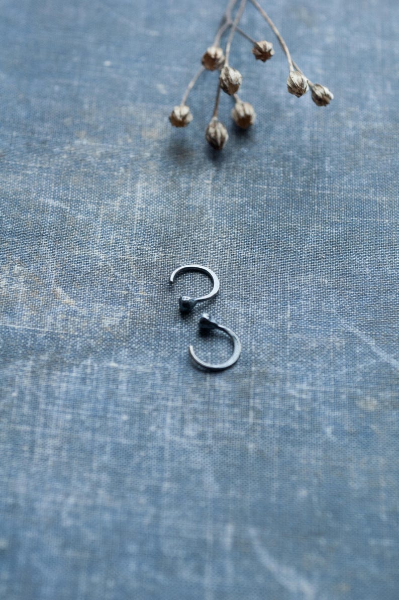 May include: Two silver hoop earrings with a small ball at the end of each hoop. The earrings are on a blue textured fabric background.