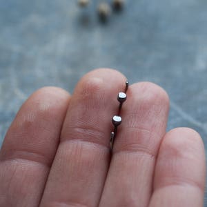 May include: Two silver stud earrings with square-shaped tops held in a hand.