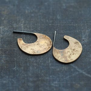 Op de afbeelding: Een paar gouden oorbellen in een halve maan vorm. De oorbellen hebben een getextureerd oppervlak en zijn gemaakt van metaal.