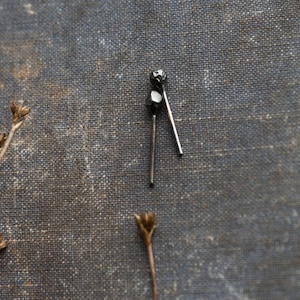 May include: Two silver metal earrings with a textured, geometric design. The earrings are on a dark grey fabric background.