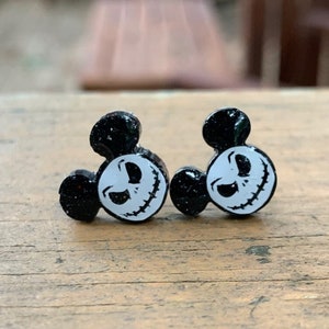 Op de afbeelding: Een paar zwarte glitter Mickey Mouse oorbellen met een wit Jack Skellington gezicht op elk oor.