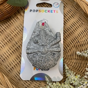 May include: A silver glitter PopSockets PopGrip featuring a cartoon cat design. The packaging includes the PopSockets logo and the text "PopGrip".