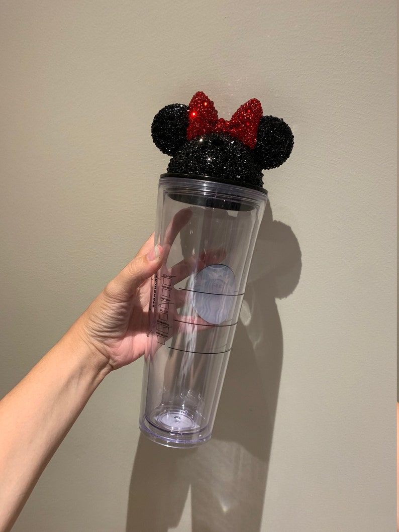 May include: A clear plastic tumbler with a black and red rhinestone Minnie Mouse lid. The lid features a black bow with red rhinestones.
