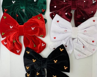 May include: Four velvet bows with different colors and embellishments. The bows are green, red, white, and black. Each bow has a different design of rhinestones.