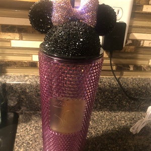 May include: A pink and black rhinestone tumbler with a Minnie Mouse lid. The lid features a black bow with pink rhinestones and black ears.