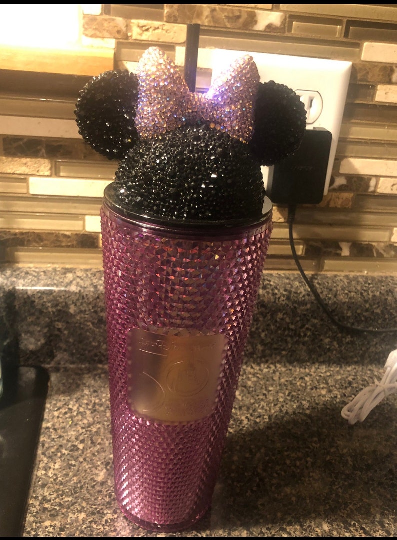 May include: A pink and black rhinestone tumbler with a Minnie Mouse lid. The lid features a black bow with pink rhinestones and black ears.