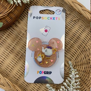Puede incluir: Un PopSockets PopGrip rosa y dorado con un fondo brillante, una tetera blanca y un pájaro amarillo. El texto "APPABLE TO CHANGEABLE" y "POPGRIP" es visible en el empaque.