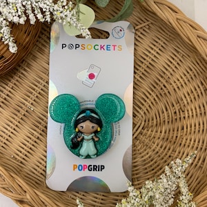 May include: A green glitter phone grip with a pop socket featuring a cartoon image of Princess Jasmine from Disney's Aladdin. The text "POPSOCKETS" and "POPGRIP" are on the packaging.