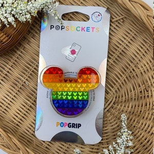 May include: A rainbow-colored PopSockets PopGrip featuring a Mickey Mouse silhouette with a holographic finish. The PopGrip is packaged on a white card with the text "POPSOCKETS" and "POPGRIP".