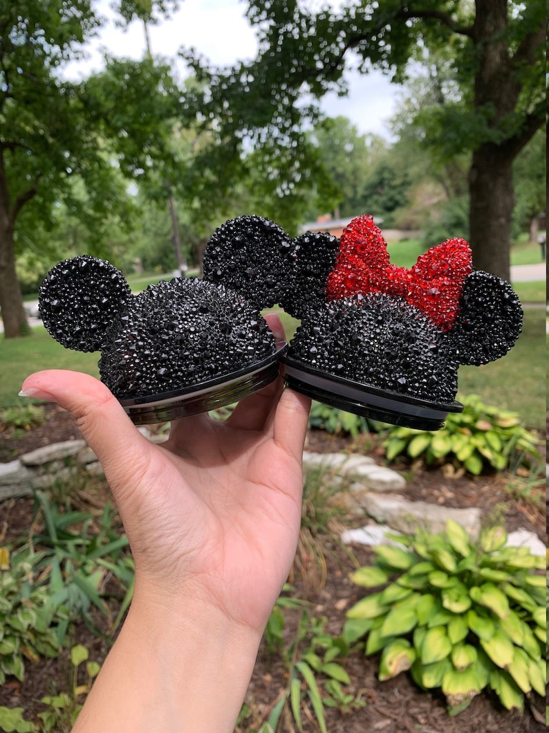 May include: Two black and red rhinestone-covered Mickey Mouse ears. The ears are for a tumbler lid.