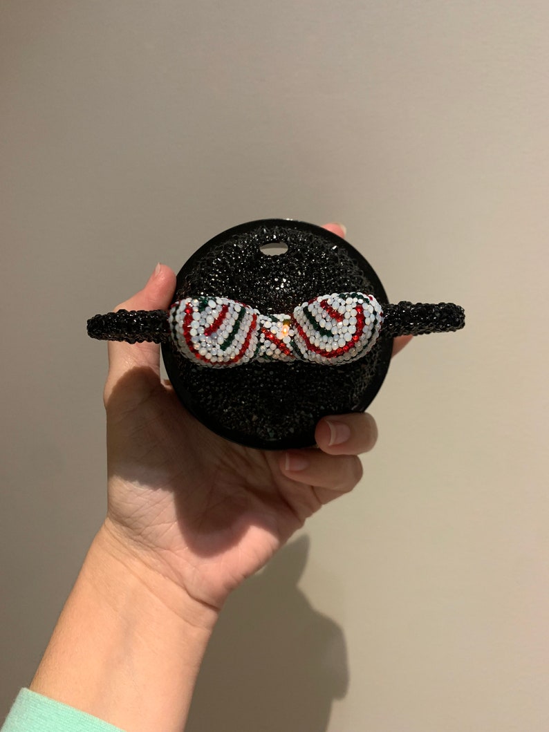 May include: A black and white rhinestone Mickey Mouse head with a red and green striped bow.