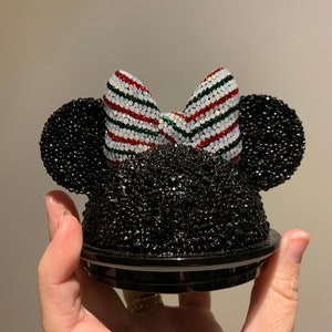 May include: Black and white Minnie Mouse ears with a red, white and green striped bow. The ears are covered in rhinestones.