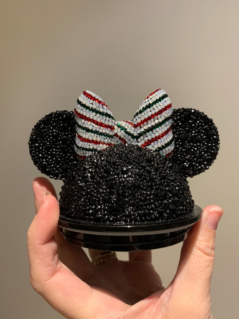 May include: Black and white Minnie Mouse ears with a red, white and green striped bow. The ears are covered in rhinestones.