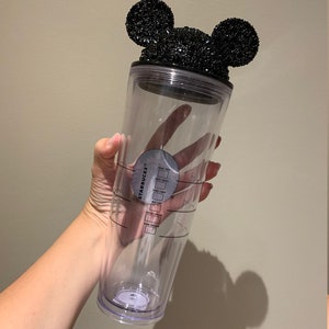 May include: Clear plastic reusable Starbucks tumbler with a black Mickey Mouse ears lid covered in black rhinestones. The tumbler has measurement markings for sugar, cream, shots, milk, and total ounces.