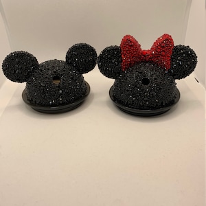 May include: Two black and red rhinestone covered bottle stoppers with Mickey Mouse ears. One stopper has a red rhinestone bow on top of the ears.