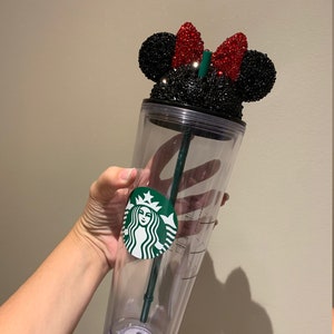 May include: A clear plastic tumbler with a black and red rhinestone Minnie Mouse lid. The tumbler has a green Starbucks logo on the side.