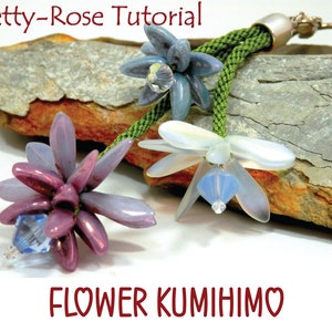 May include: A close-up of a green cord with three flower charms. The flowers are made of iridescent beads and have crystal accents. The cord has a silver clasp and ring. The text "FLOWER KUMIIMO" is written in red below the flowers.