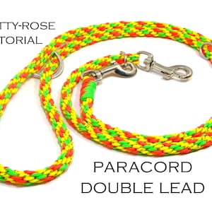 Könnte beinhalten: Eine doppelte Hundeleine aus geflochtener Paracord in Rot, Gelb und Grün. Die Leine hat einen Griff, zwei Metallringe und zwei Metallverschlüsse. Der Text auf dem Bild lautet "A Betty-Rose Tutorial" und "Paracord Double Lead."