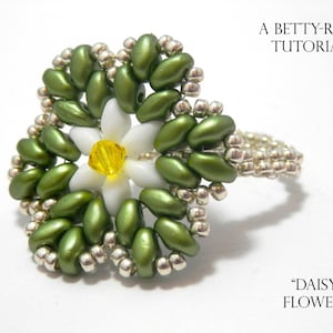 May include: A green and white beaded ring with a daisy flower design. The ring is made with seed beads and features a yellow center bead. The ring is labeled "A Betty-Rose Tutorial" and "Daisy Flower".
