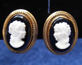 Könnte beinhalten: Ein Paar goldfarbene Kameenohrringe mit schwarzem Emaille und weißen Kameenporträts. Die Kameen sind oval geformt und zeigen das Profil einer Frau.