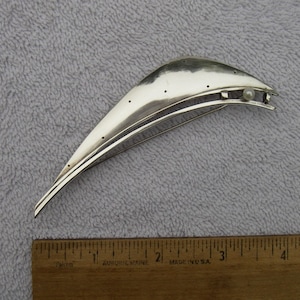 Könnte beinhalten: Eine silberne Brosche in Form eines Halbmondes mit einem kleinen Perlenakzent. Die Brosche ist etwa 7,5 cm lang.