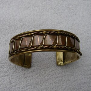 May include: A copper and brass cuff bracelet with a braided design. The bracelet has a hammered copper finish and a twisted wire design.