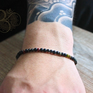 May include: A black beaded bracelet with small red, green, and gold beads interspersed throughout.