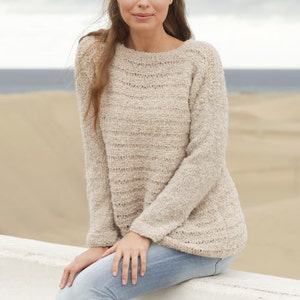 May include: A light beige knit sweater with a crew neck and long sleeves. The sweater has a textured appearance and is worn with light blue jeans. The image includes the text "DROPS DESIGN" and "www.garnstudio.com".