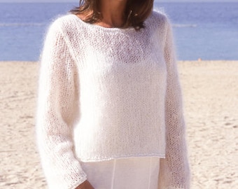 Può includere: Una donna indossa un maglione bianco a maniche lunghe con scollo tondo. Il maglione è realizzato in un materiale morbido e strutturato. L'immagine include anche il testo "DROPS DESIGN" e "www.garnstudio.com".